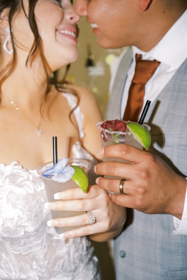 bride and groom holding signature cocktails with lime and flower garnishes