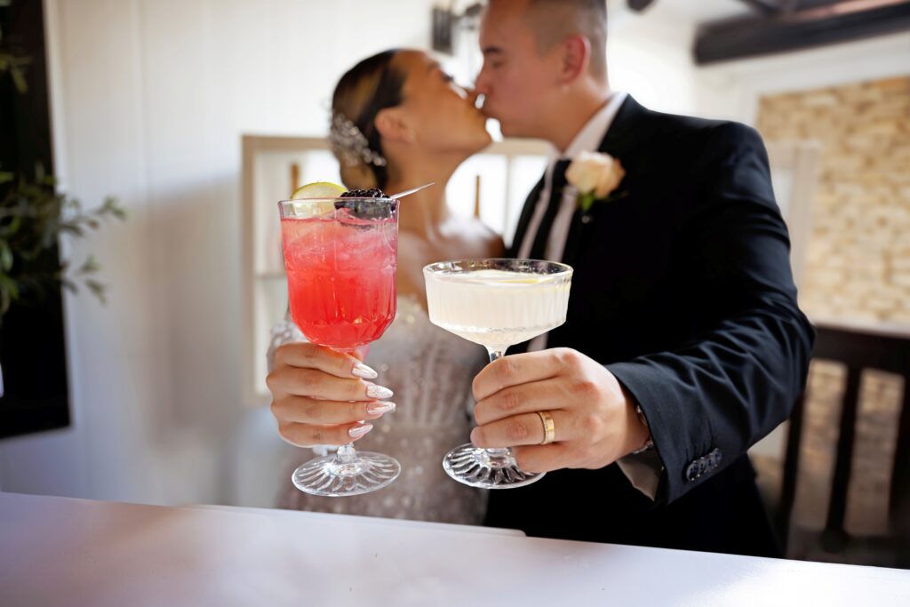 Bride and Groom share a kiss and toasting with handcrafted cocktails at a wedding bar, luxury bartending service in Dallas Fort Worth